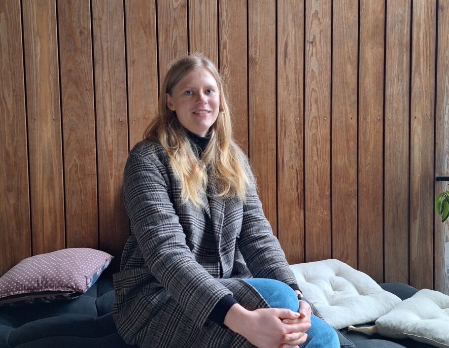 Clara sidder iført jakke og smiler mod kameraet.