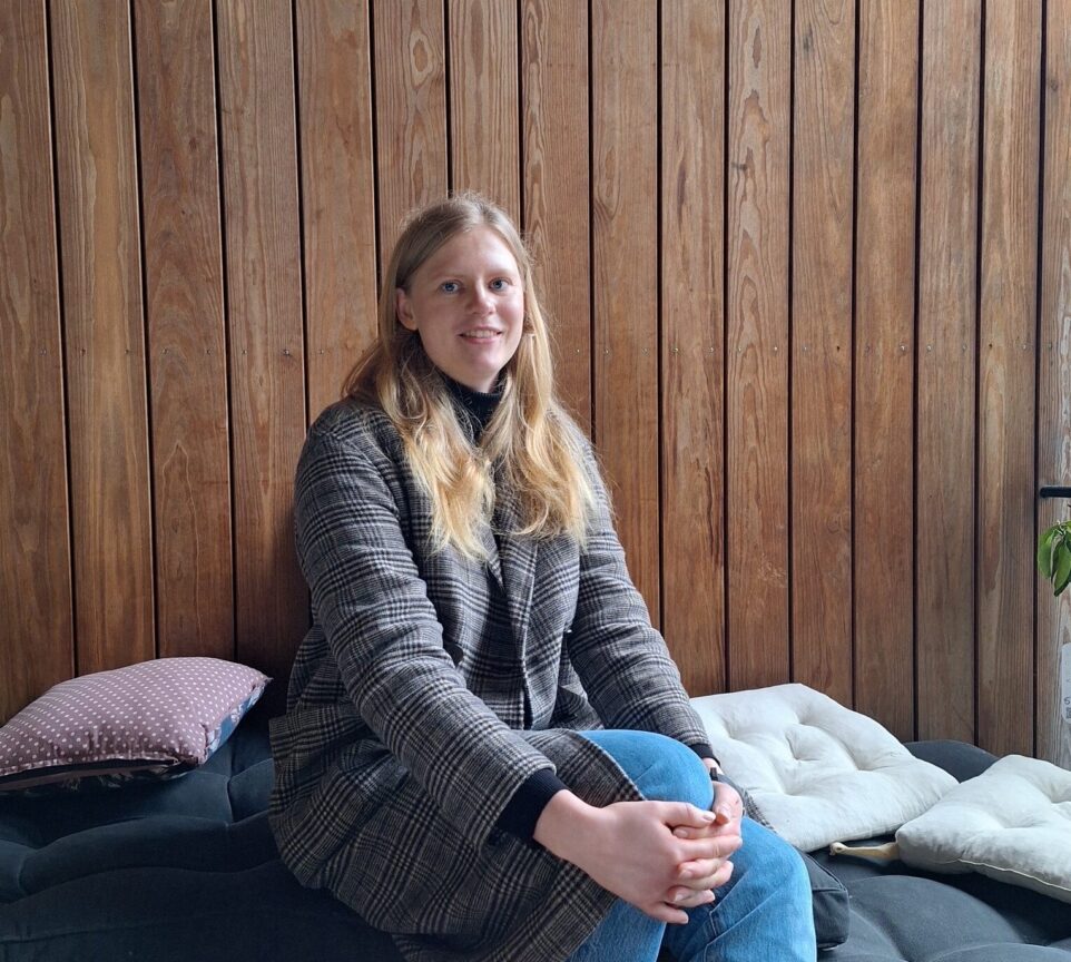 Clara sidder iført jakke og smiler mod kameraet.