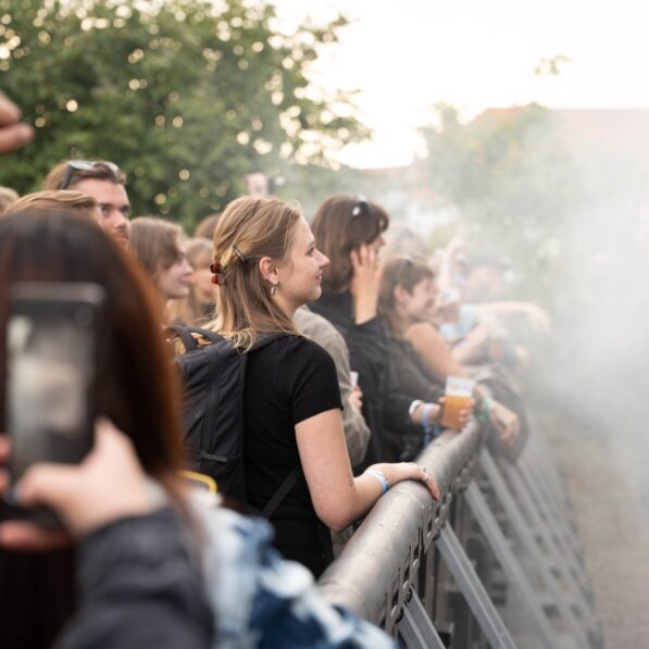 På billedet kan man se flere unge mennesker stå op langs gelænderet til en musikscene.
