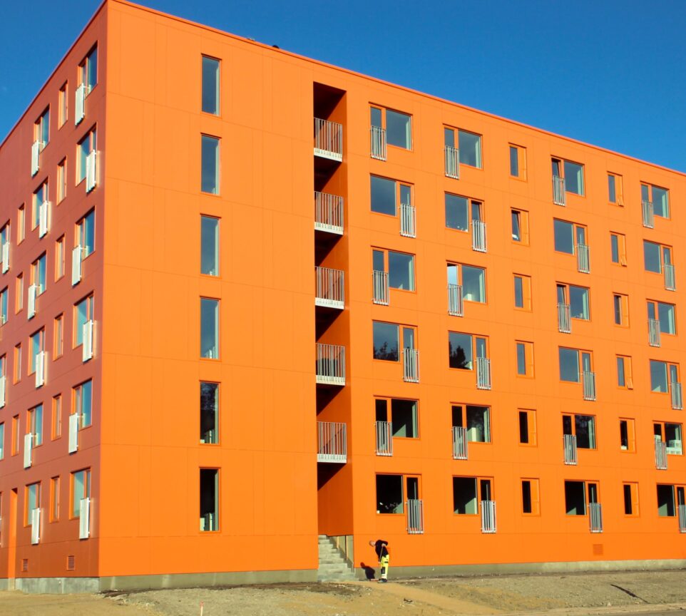 På billedet fremgår et stort, orange bygningskompleks med ungdomsboliger.
