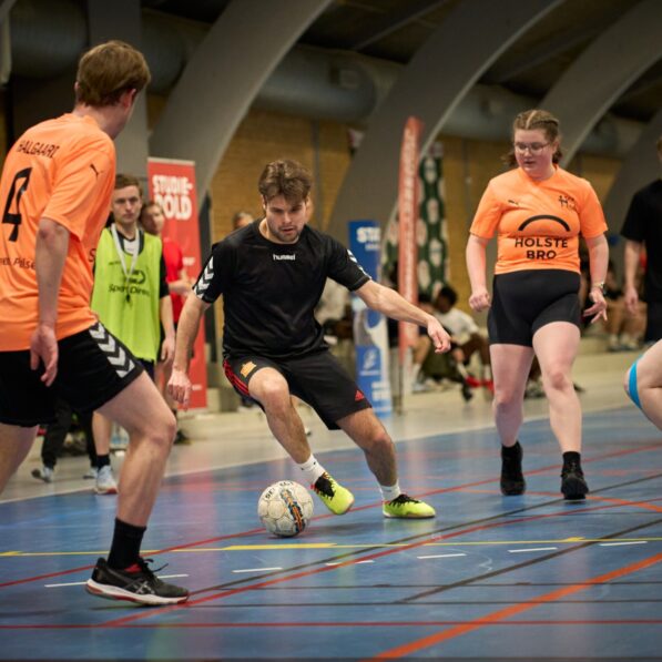 En gruppe unge mennesker er i gang med en intens fodboldkamp på en indendørs bane.