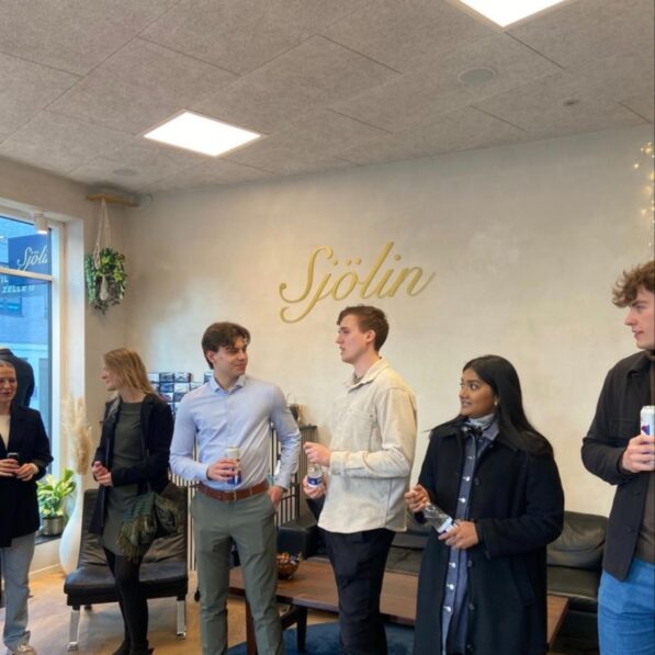 En gruppe unge mennesker iført fint tøj snakker med hinanden, med "Sjölin" i guldbogstaver på væggen bagved dem.