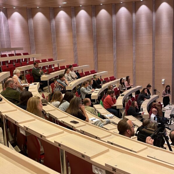 Publikummet sidder i en undervisningssal på SDU Kolding og lytter opmærksomt med. Salen har loft til loftet, samt mange pladser, der alle vender mod præsentationen.