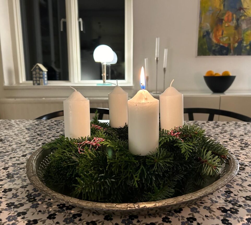 Adventkrans lavet af grene, dekoreret med fire stearinlys, bånd og ornamenter.